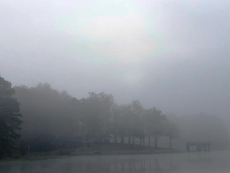 distant shoreline reflecting in water with heavy fog obscuring sun