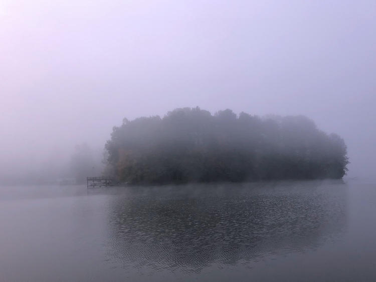 distant shoreline with trees and barely visible boat dock, smooth water, all covered with heavy fog